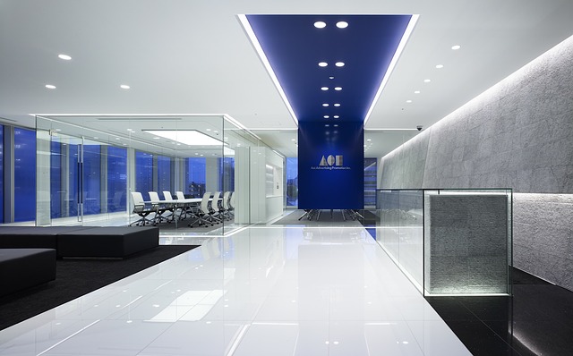 moderní prostředí, lesklá podlaha na chodbě, modrý strop s výraznými světly, v dáli bílé židle ve skleněné místnosti